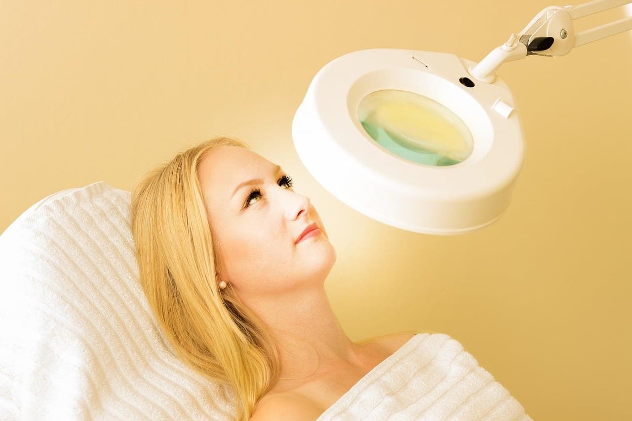 A client under a magnifier lamp in a warm aesthetics treatment room