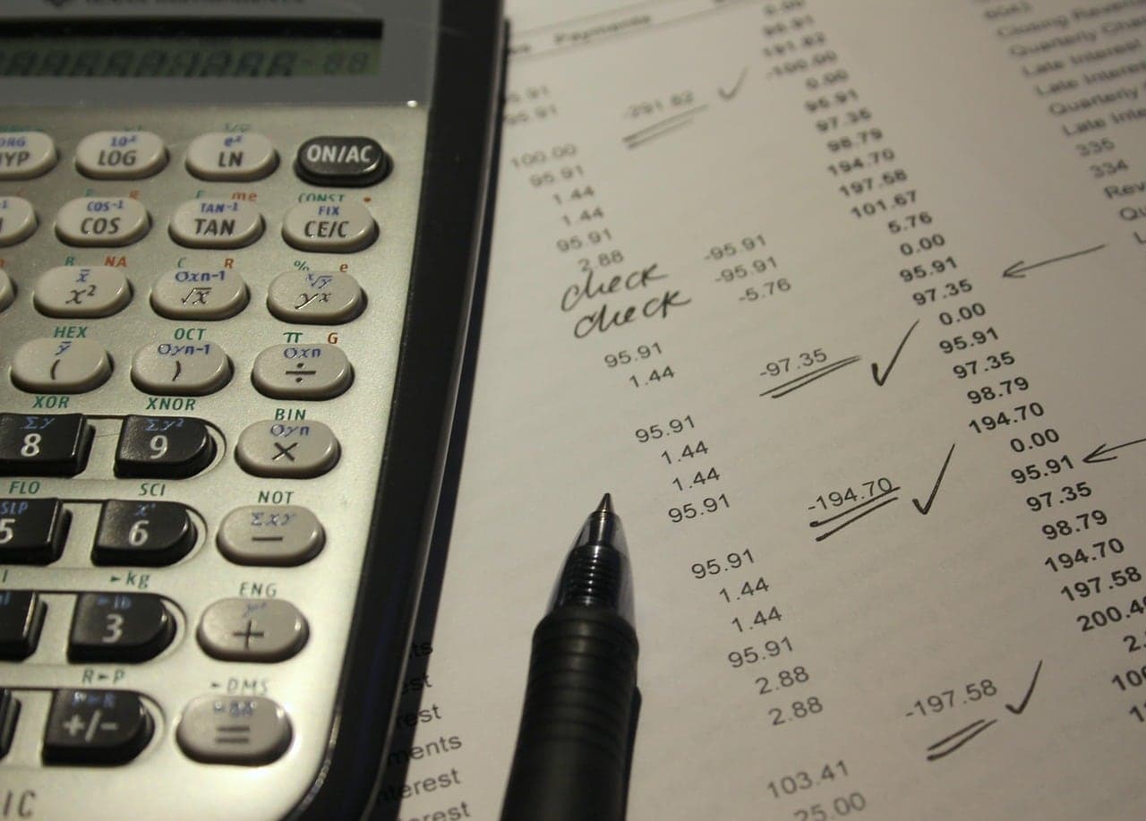 A calculator, pen and a checked statement on a desk